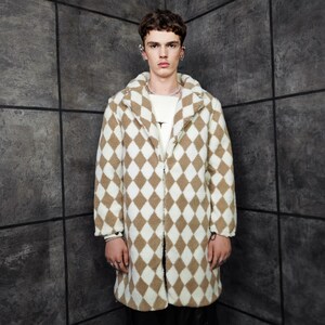 Pode incluir: Um casaco comprido e aberto com um padrão de losangos castanho e branco. O casaco tem uma gola larga e mangas compridas. É usado sobre uma camisa branca. O casaco é feito de um material macio e texturizado.