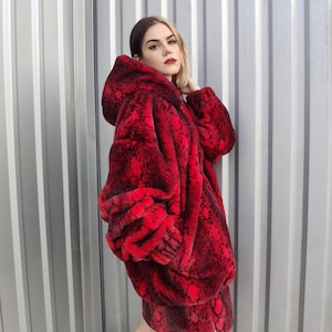 Peut inclure: Veste à capuche et jupe assortie en fausse fourrure rouge avec un motif peau de serpent. La veste et la jupe ont une fermeture éclair. L'ensemble est une déclaration de mode audacieuse.
