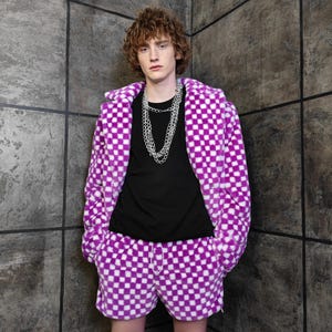 May include: A purple and white chequered fleece jacket and matching shorts. The jacket has a hood and the shorts have a drawstring. A black t-shirt and silver chain necklace complete the outfit.