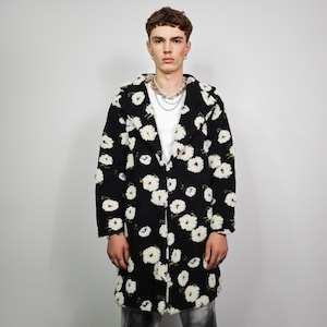 May include: A black coat with a white floral pattern. The coat has a classic lapel collar and a long, straight cut. The white flowers are scattered across the coat's surface. The coat is worn over a white t-shirt.