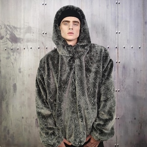 May include: A hooded faux fur jacket in a snakeskin pattern. The jacket is a mix of gray and black, with a soft, textured appearance. The hood is up, and the jacket is buttoned at the top.