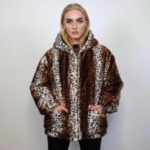 May include: A hooded faux fur coat with a leopard print pattern in shades of brown, black, and cream. The coat has a zip-up front and two front pockets. The style is oversized and cozy.