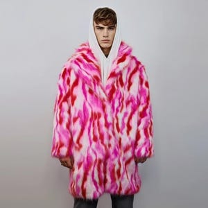 May include: A vibrant, oversized faux fur coat in shades of pink, red, and white. The coat features a wide collar and a long, flowing design. The coat is worn over a white hooded sweatshirt.