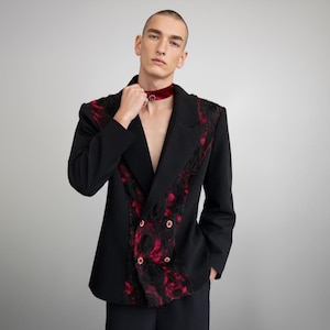 Könnte beinhalten: Schwarzer Blazer mit roter Blumenstickerei und goldenen Knöpfen. Der Blazer hat ein doppelreihiges Design und ein fallendes Revers. Ein rotes Samt-Choker mit dekorativer Mitte ist ebenfalls sichtbar.