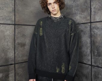May include: Black and green distressed sweater with vertical ribbing and a crew neck. The sweater has a worn look with distressed details and a spiked collar. The sleeves are long, and the sweater is paired with black pants.