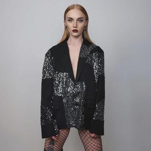 Puede incluir: Blazer negro con diseño de patchwork de lentejuelas plateadas. El blazer tiene un cuello con solapas clásico y un cierre de un solo botón. Las lentejuelas están dispuestas en un patrón geométrico, agregando un toque de glamour. Una prenda exterior elegante.