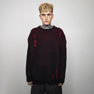 May include: A dark burgundy and black sweater with distressed details. The sweater has a ribbed texture and a black crew neck. The design includes intentional rips with red thread accents, adding a unique, edgy style to the garment.