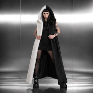 May include: A long, hooded vest with a striking split design: one side is white, the other black. The faux fur vest is sleeveless and reaches the ankles. The model is wearing a black dress and platform boots.