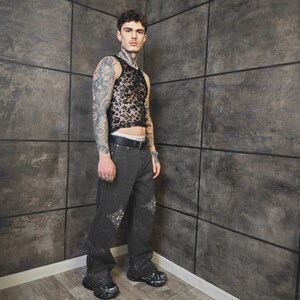 May include: A black lace tank top and black studded pants with ripped details. The pants have a wide leg fit. The outfit is paired with black shoes and a black belt.
