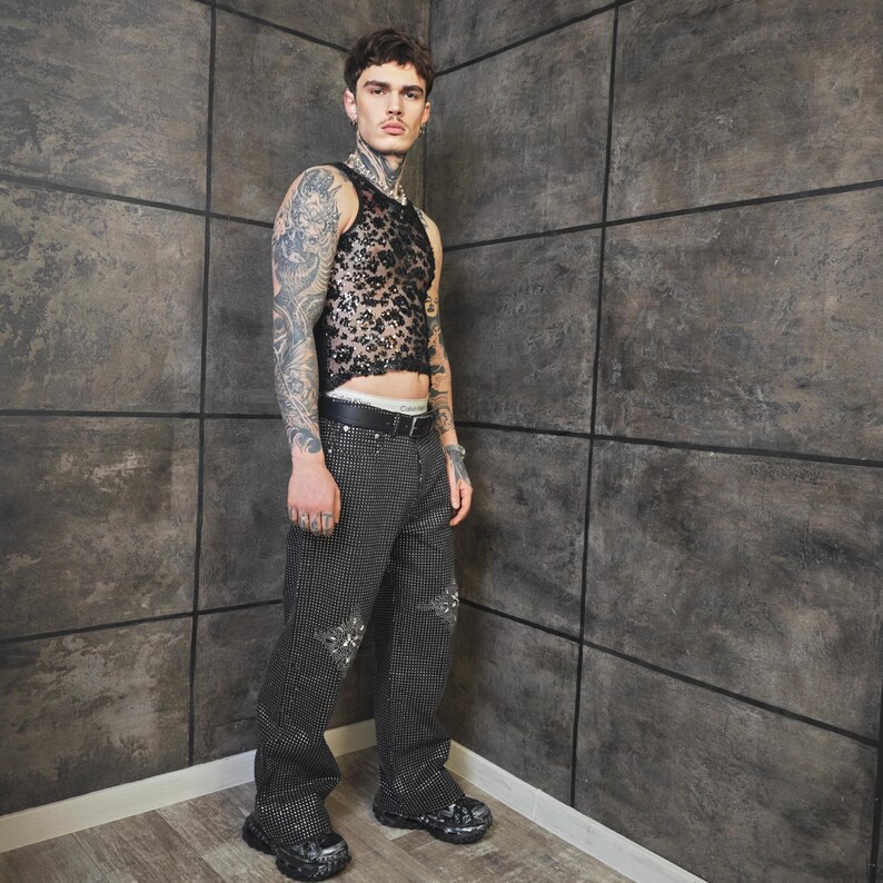 May include: A black lace tank top and black studded pants with ripped details. The pants have a wide leg fit. The outfit is paired with black shoes and a black belt.