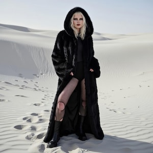 May include: A long, black faux fur coat with a large hood. The coat is worn over a black outfit, with fishnet stockings and black boots. The background is a desert landscape with white sand.
