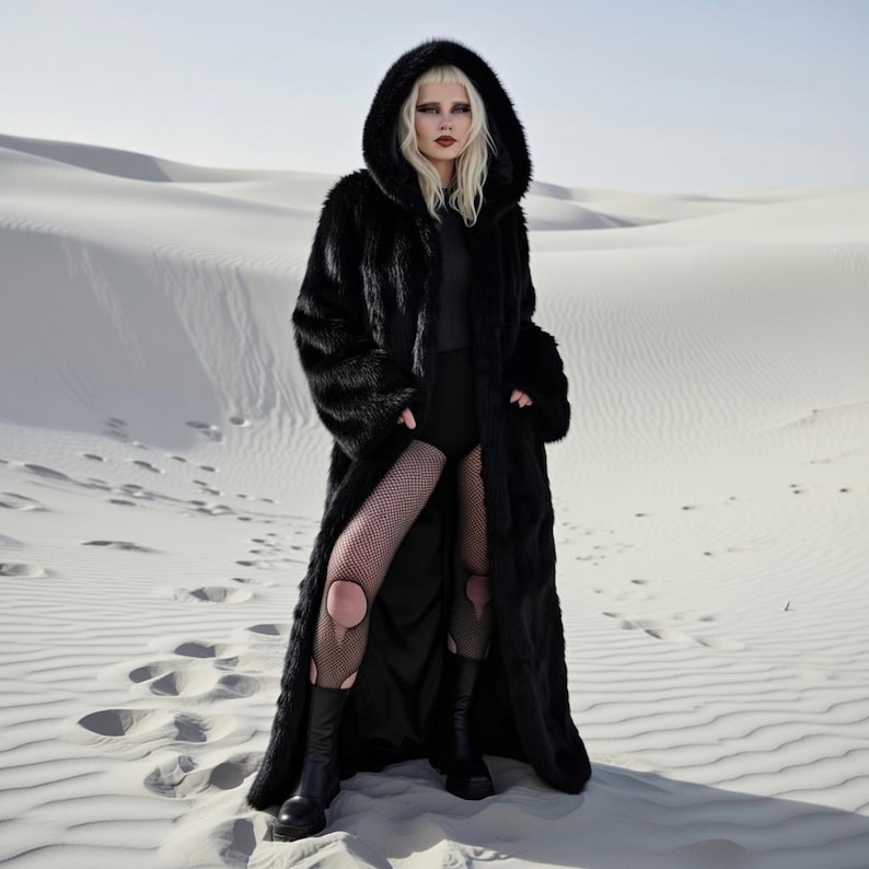 May include: A long, black faux fur coat with a large hood. The coat is worn over a black outfit, with fishnet stockings and black boots. The background is a desert landscape with white sand.