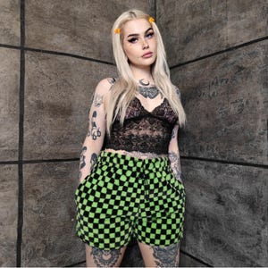 May include: A black lace crop top and green and black checkered shorts. The shorts have a drawstring waist and pockets. The outfit is casual and stylish.