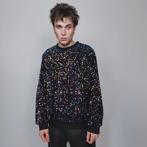 Può includere: Felpa nera con paillettes e maniche lunghe. Le paillettes sono iridescenti, riflettendo più colori. La felpa ha girocollo e polsini neri. L'indumento è un top casual.