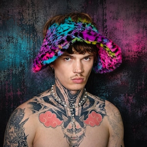 Może przedstawiać: Kapelusz typu bucket hat z szerokim rondem wykonany ze sztucznego futra, ozdobiony wyrazistym, wielokolorowym wzorem w panterkę w odcieniach neonowego różu, elektryzującego błękitu i jaskrawej żółci. Kapelusz ma miękką, puszystą fakturę i zaokrągloną główkę.