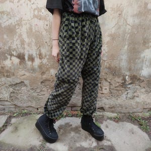 May include: Green and black chequered pattern trousers with a soft, textured appearance. The trousers have a relaxed fit and are paired with black platform trainers. The style suggests a casual, streetwear aesthetic.