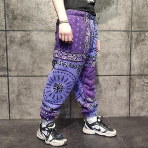 Könnte beinhalten: Lila und lavendelfarbene Fleece-Jogginghose mit Muster, Kordelzug in der Taille und elastischen Bündchen. Die Hose hat ein sich wiederholendes geometrisches Design und wird mit schwarz-weißen Turnschuhen kombiniert.