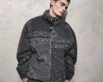 May include: A gray fleece jacket with a high collar and a full-length zipper. The jacket features a detailed paisley pattern in darker gray tones. The model is wearing the jacket, which appears to be part of a matching set.