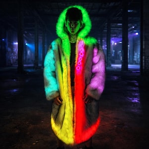 May include: A long, open faux fur coat with a vibrant, color-blocked design. The coat features a neon green hood and transitions through shades of teal, yellow, red, and purple. The coat is worn in a dark, industrial setting.