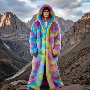 Può includere: Un lungo cappotto con cappuccio in un vibrante arcobaleno di colori, tra cui rosa, blu, verde e giallo. Il cappotto in ecopelliccia è indossato all'aperto sullo sfondo di montagne e un cielo nuvoloso. Il cappotto ha un design lungo e fluido.