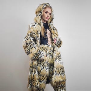 May include: A leopard print faux fur coat with a hood and matching trousers. The coat has a longline design, and the trousers are high-waisted. The outfit's colours are tan, black, and cream. The ensemble is a bold fashion statement.