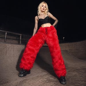 Puede incluir: Pantalones de piel sintética de color rojo brillante con cintura de cordón, combinados con un top bustier negro corto y una camiseta de malla negra de manga larga con patrón de pedrería, junto a zapatos de plataforma negros gruesos.
