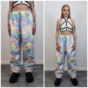 Puede incluir: Pantalones de ch&aacute;ndal de piel sint&eacute;tica de color pastel con cintura con cord&oacute;n. Los pantalones presentan un estampado tie-dye en tonos azules, amarillos, rosas y morados. La modelo lleva zapatos de plataforma negros y un top corto blanco con detalles de arn&eacute;s negro.