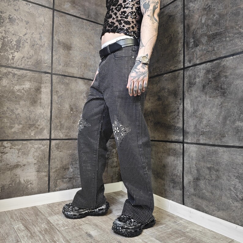 May include: Black and white patterned pants with decorative embellishments. The pants have a wide leg design and are paired with chunky platform shoes. The pants are covered in small white dots.