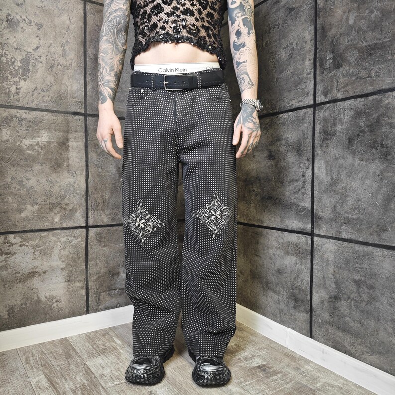 May include: Black and white patterned pants with decorative embroidery on the front. The pants have a wide leg design and are paired with black shoes. The pants are part of a fashion ensemble.