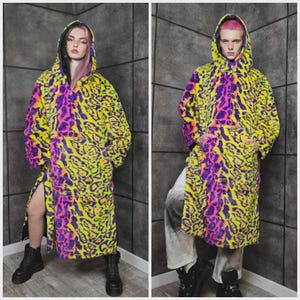 May include: Two images side-by-side of hooded coats. The coats have a neon yellow, purple, and black leopard print design. The coats are long, with a slit up the side. The models are wearing black boots.