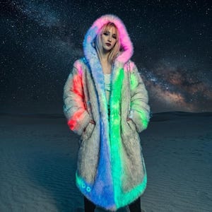 May include: A long, hooded coat with a faux fur exterior. The coat features a color gradient of pink, blue, and green along the edges and hood. The coat has pockets and is worn in a desert setting with a starry night sky background.