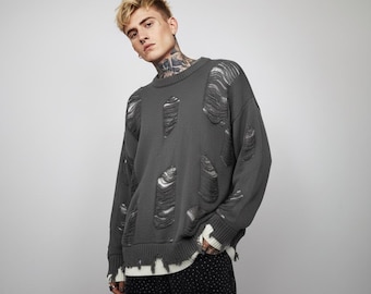 May include: A charcoal gray sweater with distressed detailing. The sweater features large, intentionally ripped sections across the front and sleeves. The cuffs and hem are finished with a white trim. The sweater is a relaxed fit.