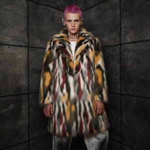 Op de afbeelding: Een lange, veelkleurige imitatiebontjas. De jas heeft een patroon van verticale strepen in tinten geel, rood, grijs, zwart en wit. De jas heeft een brede kraag en een knielange snit, wat een gedurfde mode-uitspraak oplevert.