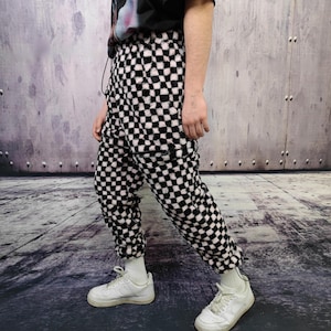 May include: Black and white chequered fleece sweatpants with a drawstring waist. The trousers are worn with white trainers and socks. The style is casual and comfortable.