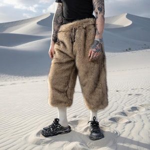 Può includere: Pantaloni corti in finta pelliccia marrone con coulisse. I pantaloni sono abbinati a scarpe da ginnastica con motivi bianchi e neri e calzini bianchi. La persona è in piedi in un paesaggio desertico.