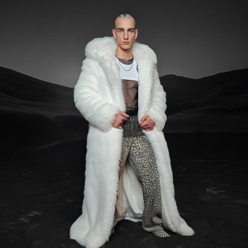 Peut inclure: Un long manteau en fausse fourrure blanche avec une grande capuche. Le manteau est port&eacute; sur un haut blanc, une chemise en r&eacute;sille noire et un pantalon &agrave; imprim&eacute; l&eacute;opard. Le fond est un paysage sombre et monochrome.