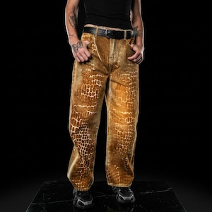 Può includere: Pantaloni marroni e beige fantasia con cintura nera. I pantaloni hanno un design unico a forma di rettile. La modella indossa una canotta nera e scarpe da ginnastica nere. I pantaloni sono in materiale morbido.