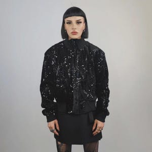 This embellished varsity jacket is the definition of dark glamour. The gloss glitter sequins create an unforgettable shiny effect. Styled as an oversized cropped blazer or a short bomber, this unisex embellished piece is ready for the club or a festive gathering. A durable, show-stopping coat for your boldest maximalist ensembles, providing the essential sparkle for any disco look.