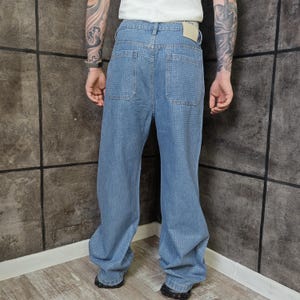 May include: Light blue denim jeans with a textured pattern. The jeans have a relaxed fit, pockets on the back, and a classic five-pocket design. The jeans are worn with black shoes.
