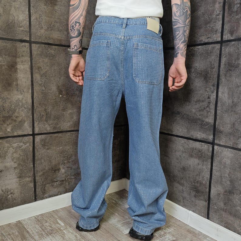 May include: Light blue denim jeans with a textured pattern. The jeans have a relaxed fit, pockets on the back, and a classic five-pocket design. The jeans are worn with black shoes.