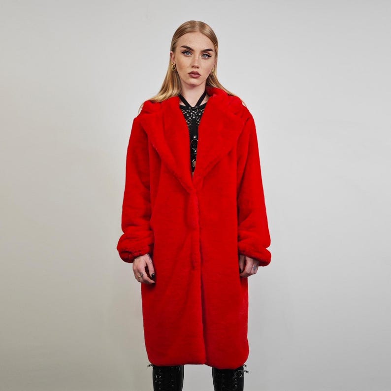 May include: A vibrant red faux fur coat with a wide collar and long sleeves. The coat is knee-length and has a soft, plush texture. The model is wearing black boots. This outerwear is perfect for cold weather.