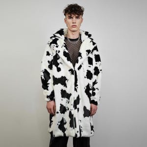 May include: A long, faux fur coat with a cow print pattern in black and white. The coat has a large collar and a long, straight cut. The coat is open in the front and appears to be made of a soft, plush material.