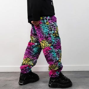 May include: Vibrant leopard print trousers in pink, purple, yellow, and teal. The trousers are worn with black platform shoes. The soft, fuzzy texture of the trousers is visible.