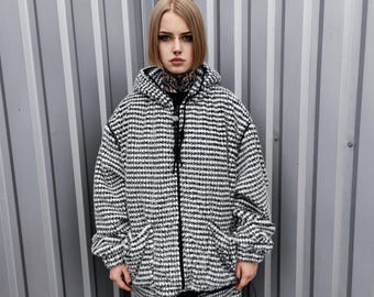 Könnte beinhalten: Eine weiße und schwarze karierte Kapuzenjacke mit Reißverschluss. Die Jacke hat eine lockere Passform und ist aus einem weichen, flauschigen Material gefertigt.