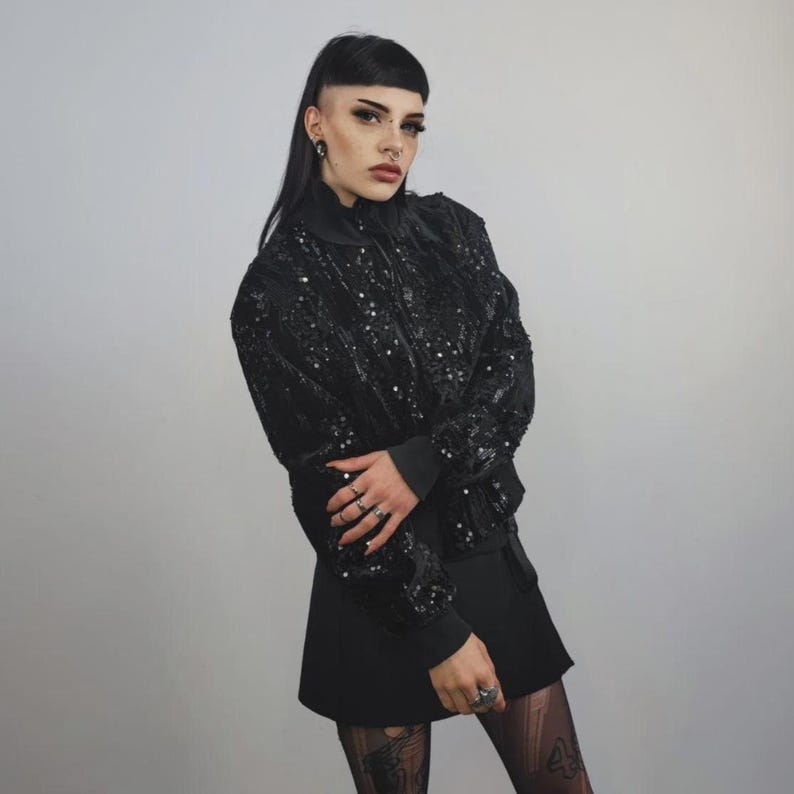 This embellished varsity jacket is the definition of dark glamour. The gloss glitter sequins create an unforgettable shiny effect. Styled as an oversized cropped blazer or a short bomber, this unisex embellished piece is ready for the club or a festive gathering. A durable, show-stopping coat for your boldest maximalist ensembles, providing the essential sparkle for any disco look.