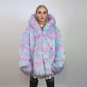 Könnte beinhalten: Ein Kapuzenmantel aus Kunstfell in Pastelltönen. Das Kleidungsstück hat rosa, blaue und violette Streifen. Der Mantel hat weite Ärmel und eine lockere Passform, ideal als auffälliges Kleidungsstück.
