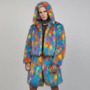 Op de afbeelding: Een kleurrijke set van een jas met capuchon en een korte broek van imitatiebont. De jas en korte broek zijn een levendige mix van blauw, oranje, geel en paars. De jas heeft een korte snit.