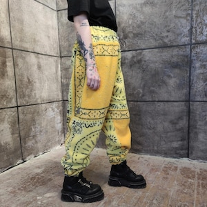 Könnte beinhalten: Gelbe Fleece-Jogginghose mit schwarzem Paisley-Muster. Die Hose hat einen Kordelzug in der Taille und elastische Bündchen. Die Person im Bild trägt schwarze Plateau-Stiefel und ein schwarzes T-Shirt.