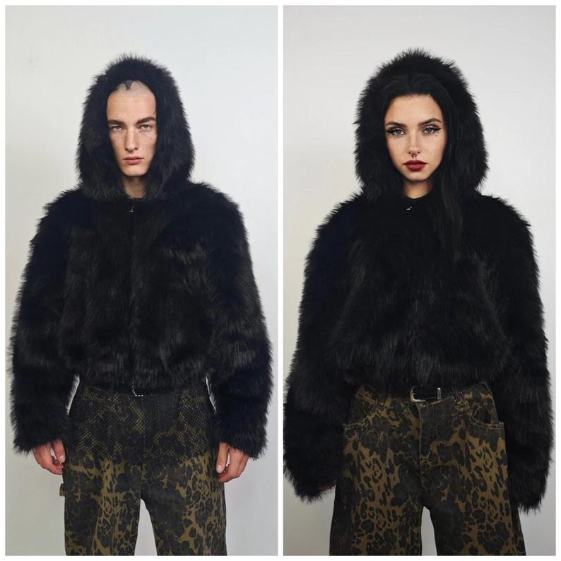 May include: A black faux fur hooded jacket with a zip-up front. The jacket has long sleeves and a cropped length. The model is wearing patterned pants. The jacket is a statement piece.