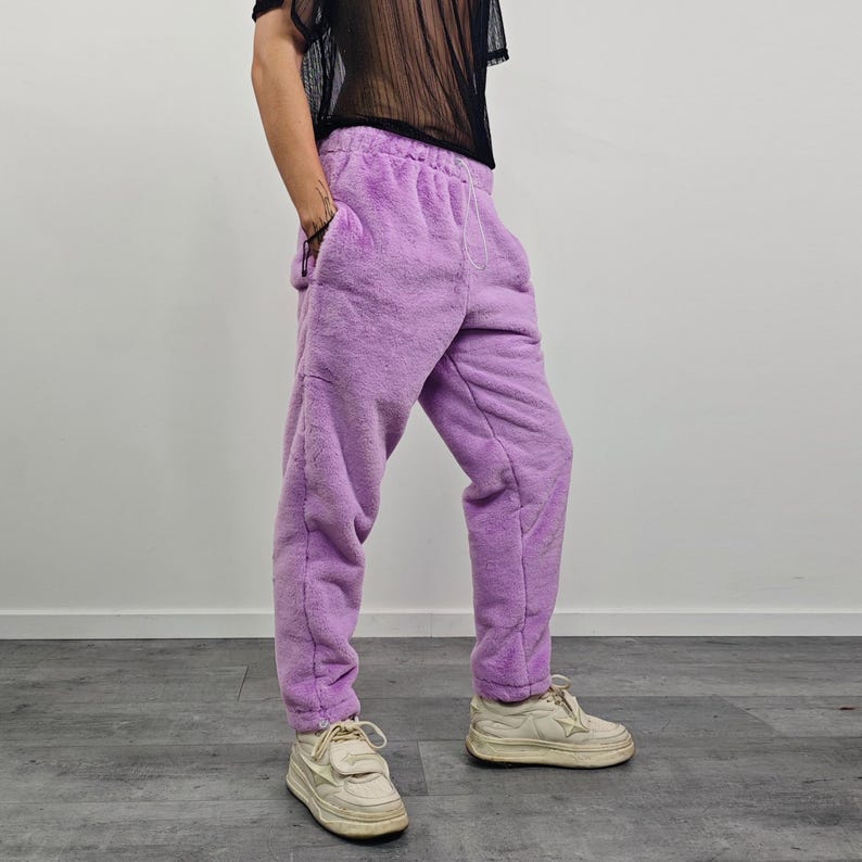 May include: Lavender-colored sweatpants with a drawstring waist and pockets. The pants have a soft, fuzzy texture. The person is wearing white sneakers.